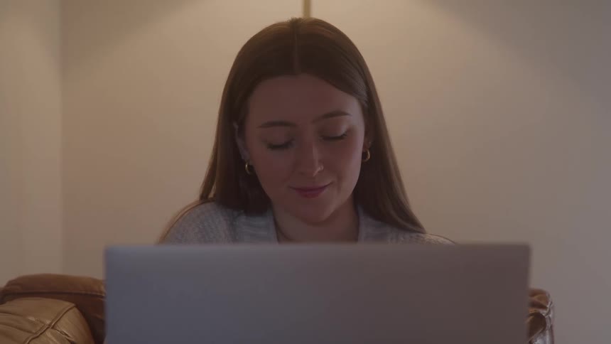 A woman sits behind a laptop faint smile forming as she reads looking relaxed and pleasantly amused