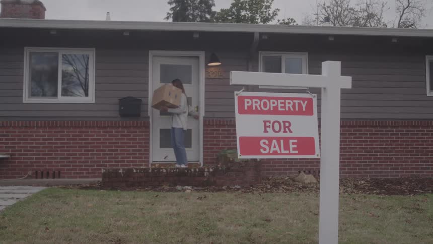 The woman is moving and carrying a box out of the home
