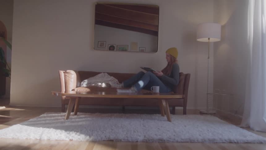 The woman walks to the couch opens a laptop as she sits