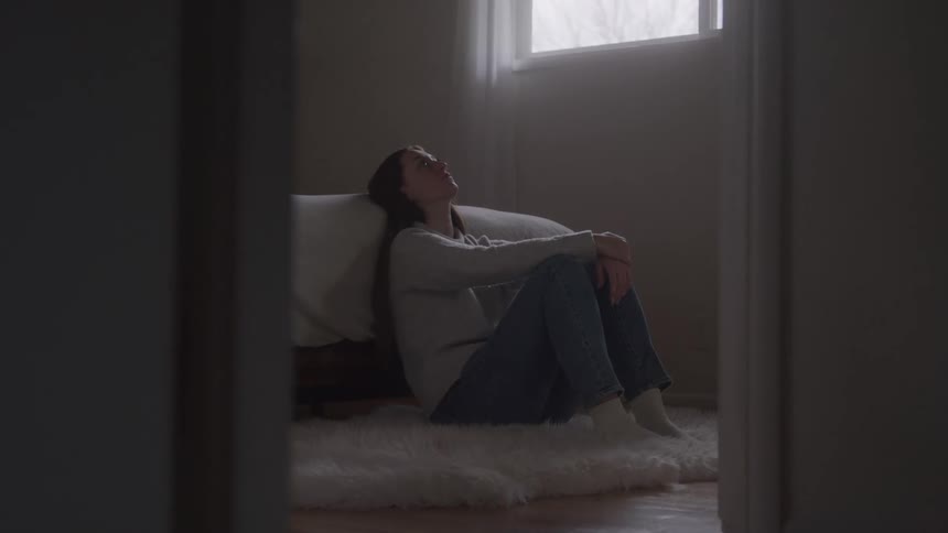 The woman is sitting on the rug looking sad