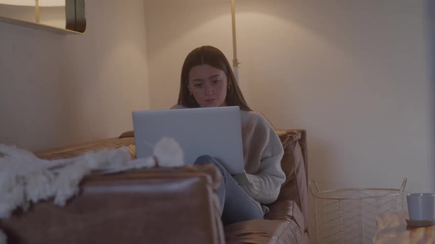 The teenager is typing on her laptop on the couch