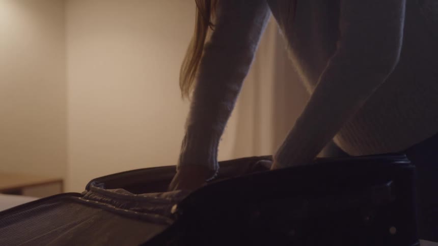 Woman in a bedroom folding clothes and packing them into a suitcase indoors during day time