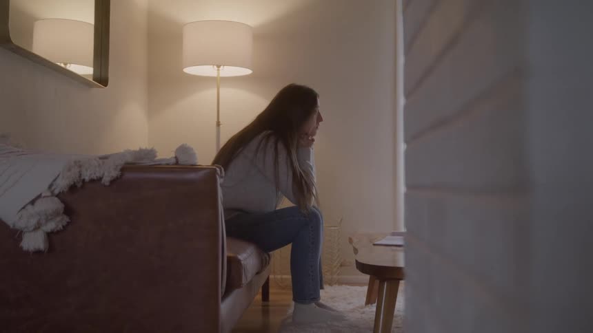 Woman sitting on the sofa watches something intently in a softly lit room
