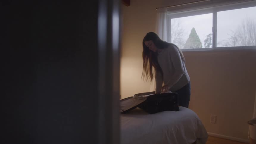 A female packs a suitcase and closes the suitcase while in a bedroom
