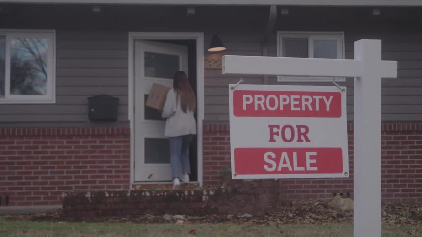 A young woman entering a house while carrying a package box during daytime