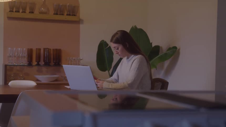 Woman sitting down in front of a laptop computer going through a small pile of papers indoors during day time
