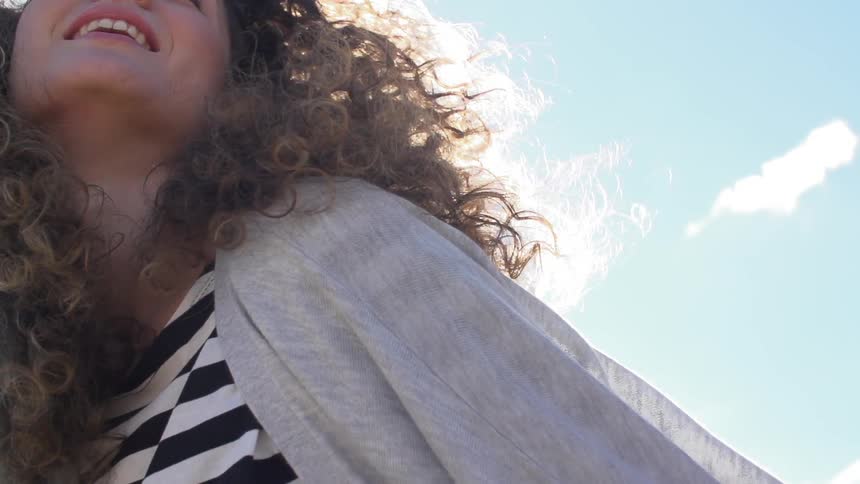 A woman tosses her hair under a sunny sky