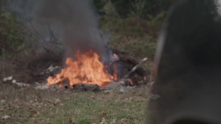 A small fire burns in a pit with smoke rising in a natural outdoor area