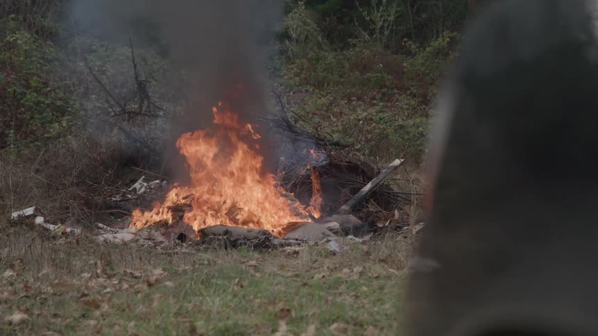 A burning fire that is smoking and surrounded by grass