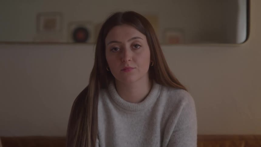 Woman in a light sweater sits on the sofa with a thoughtful downward gaze