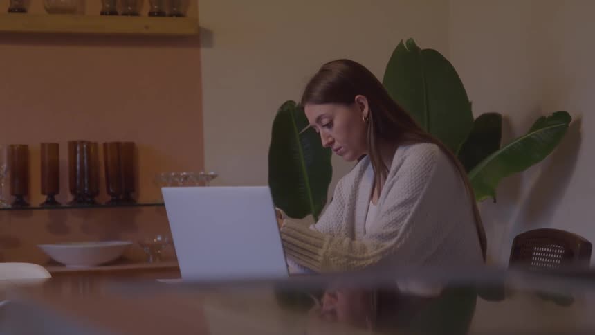 Woman sitting rests head on hand while working on laptop in a home setting