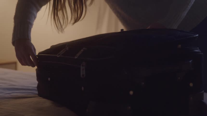 Close up of a young woman packing her luggage on a bed in a room during daytime