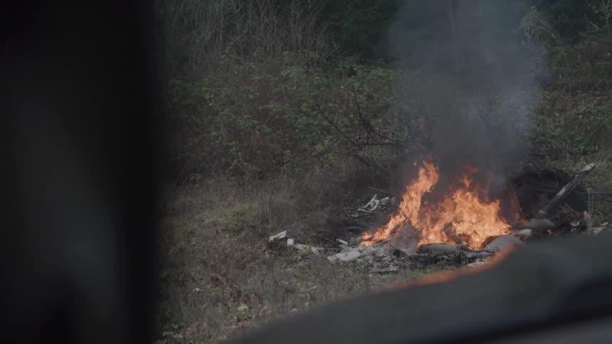 A group of items burning on the ground outdoors in a forest area during daytime