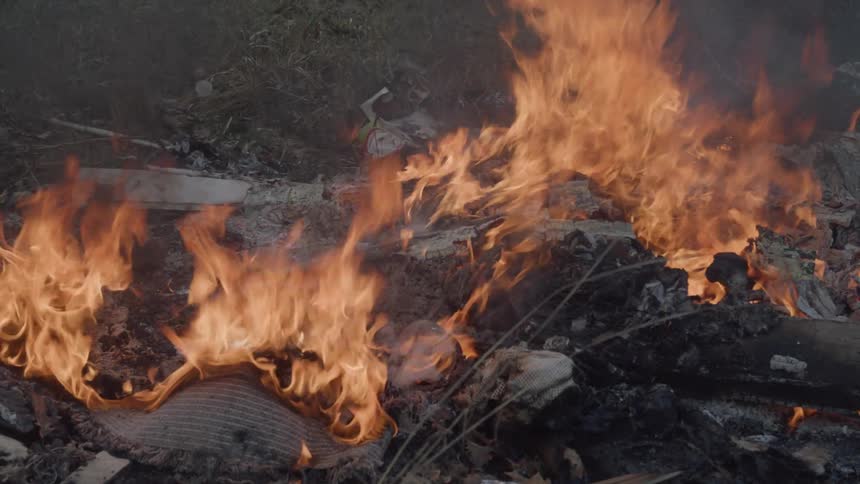 Intense fire engulfs objects and wood debris on open ground