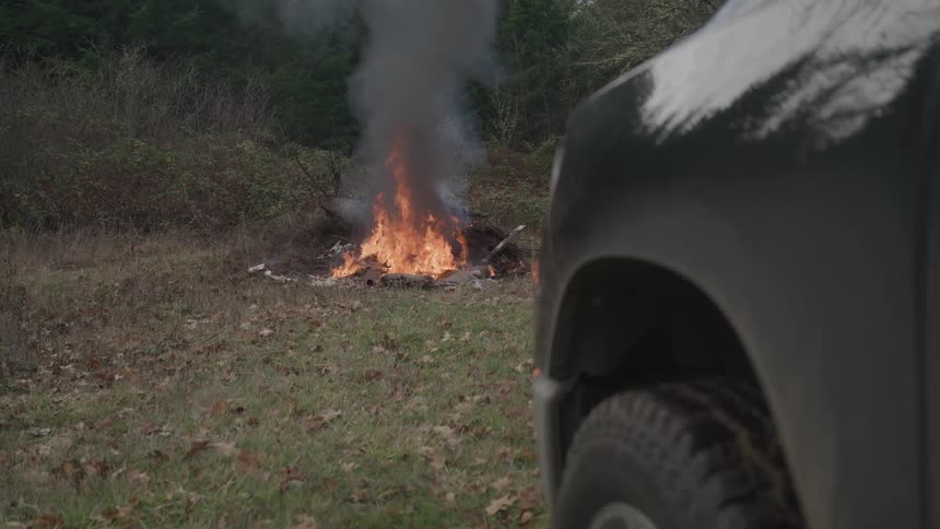 Bonfire burns outdoors while a parked vehicle appears in the foreground