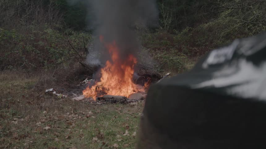 A group of items burning on the ground in a forest area during daytime