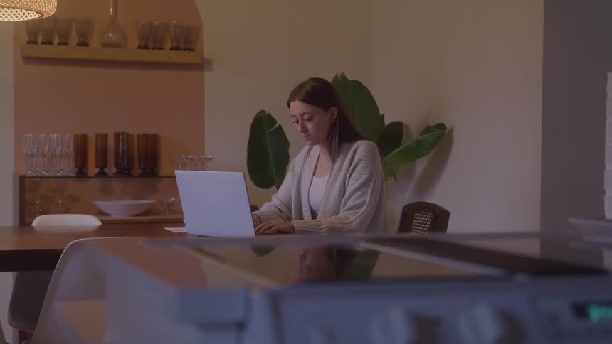 The woman sitting at the dining room table is using a laptop
