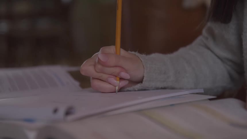 Hand holds a pencil while writing in a notebook surrounded by open books
