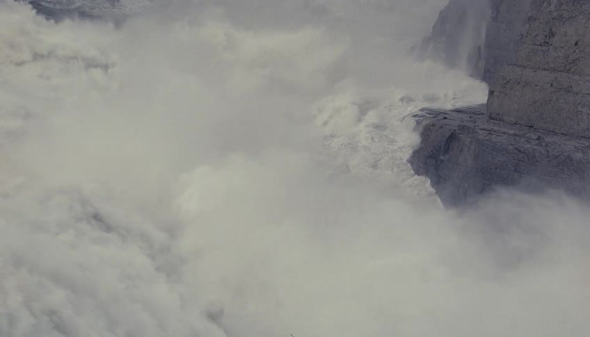 Turbulent water crashes against rocks surrounded by intense mist