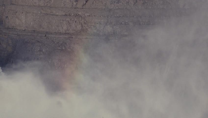 Thick mist rises in front of a rocky cliff