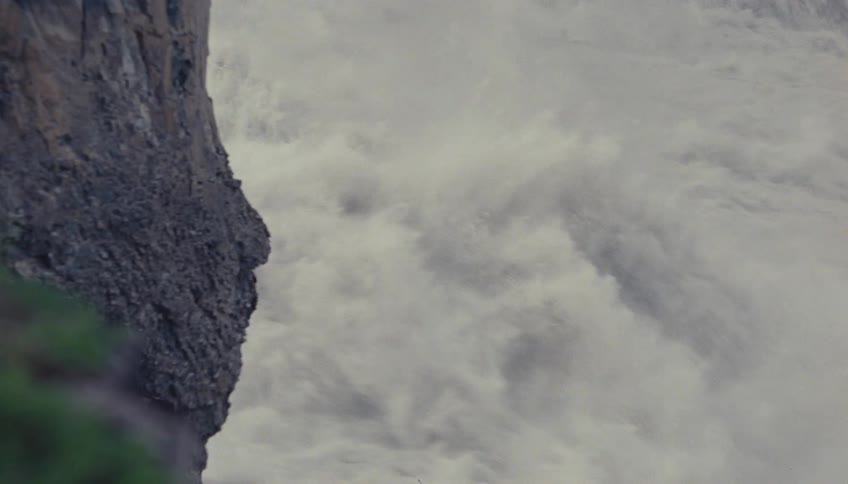 Textured rock surface occupies the left frame sharply contrasting with a massive churning volume of white water spray or mist filling the majority of the right frame