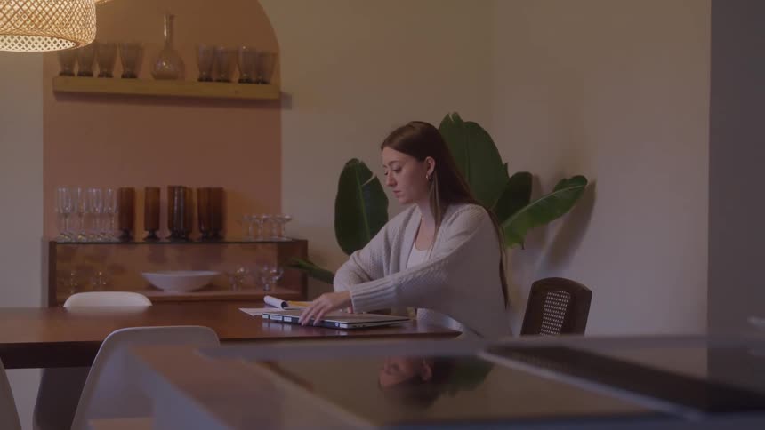 The woman sits at the dining room table and opens her laptop