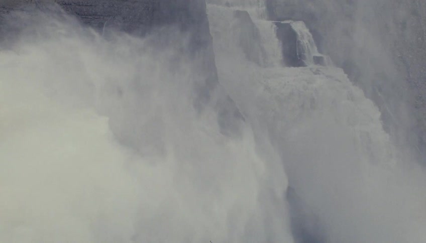 Powerful waterfall plunges down rocky cliff with heavy mist and dramatic natural setting