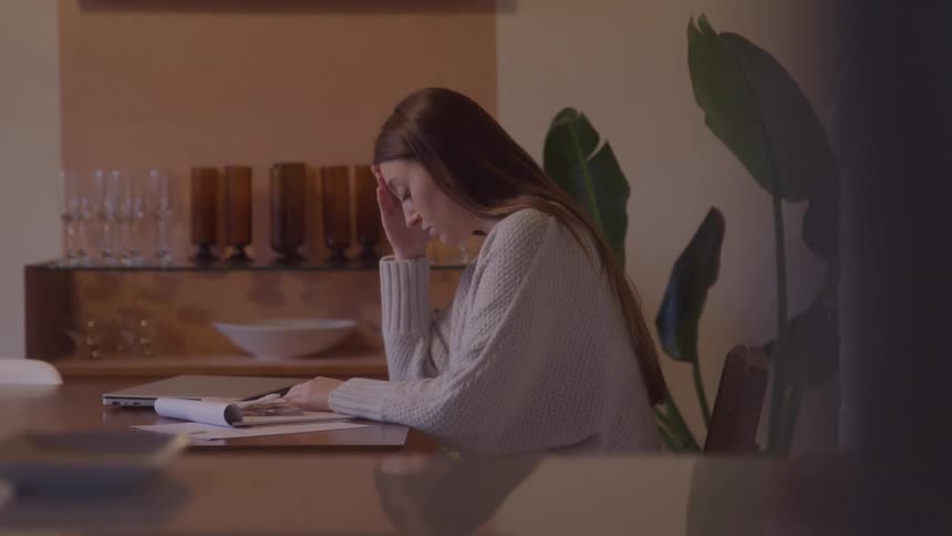 Woman studies or works with notebooks and papers on the table in a cozy home setting