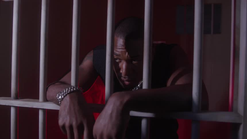 Man sitting behind bars in a room lit by red light