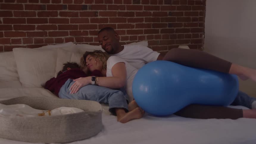 Family rest on bed beside exercise ball in room with brick wall