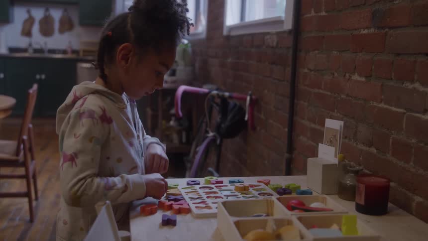 Child arranges colorful letters and shapes on table in room with brick wall