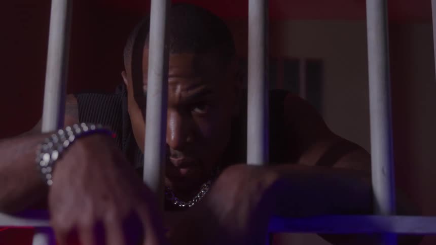 The man leans against the bars in the jail cell