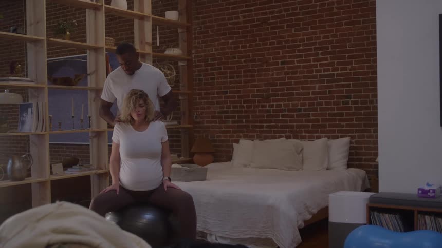 Man massaging a womans shoulders while she sits on a yoga ball