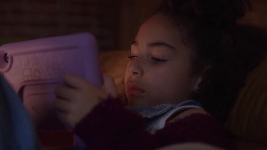 The girl is using a tablet while laying down