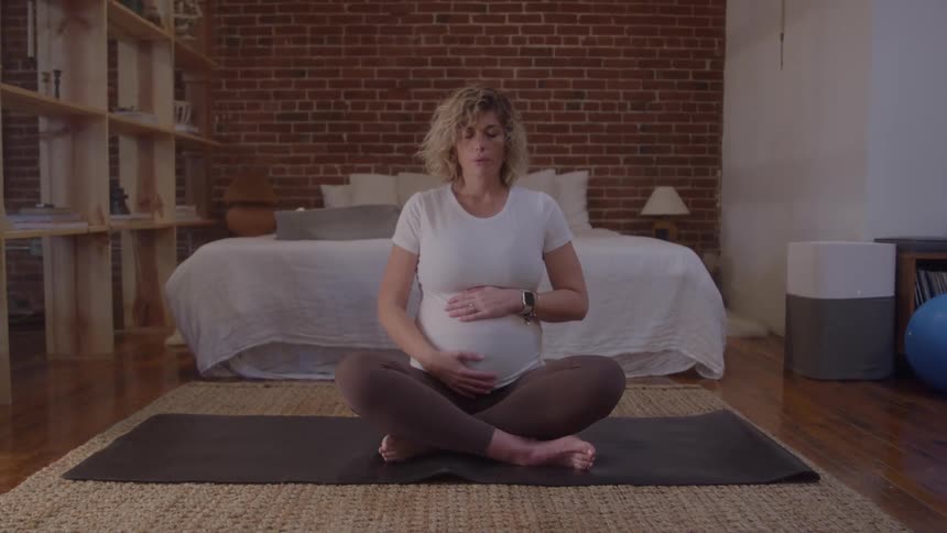 A young pregnant woman rubbing her belly while sitting on the floor in a bedroom during daytime
