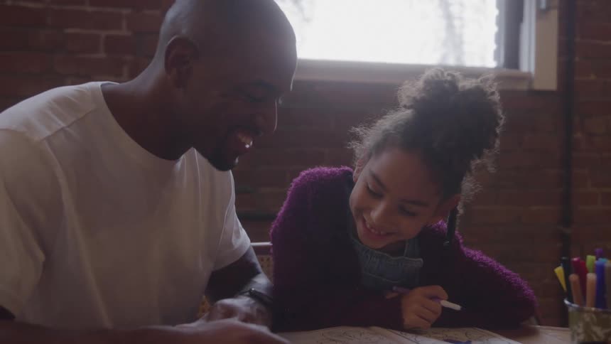 Man and smiling girl interact with pen at table in room with brick wall