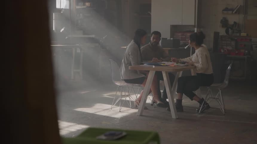 Three people seated around a table in a naturally lit space engaged in discussion or collaborative work
