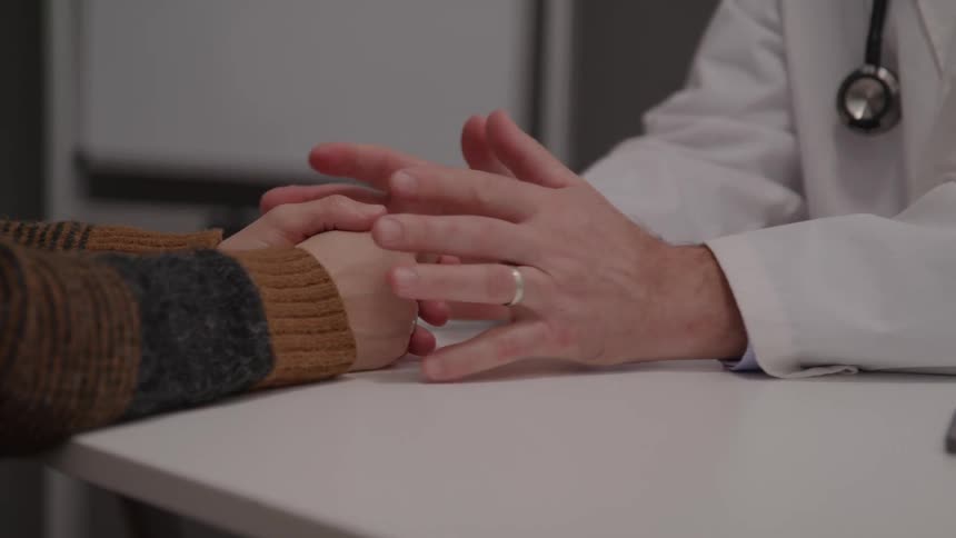 A doctor wearing a stethoscope and a wedding ring encourages a patient in the office