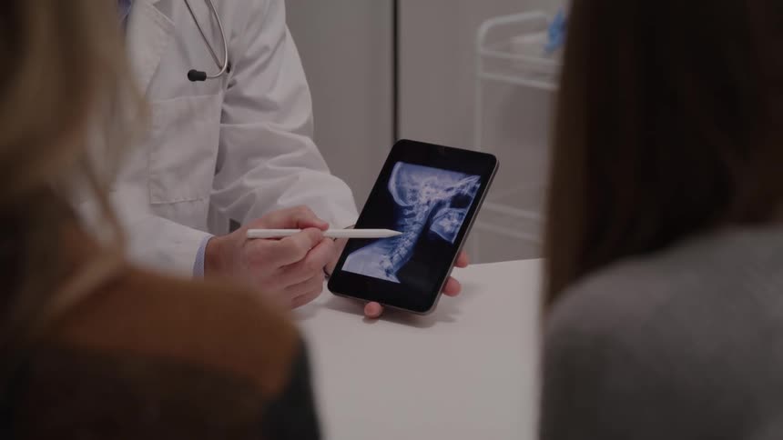 A male doctor explaining radiology scan findings to two women on a tablet device in an office