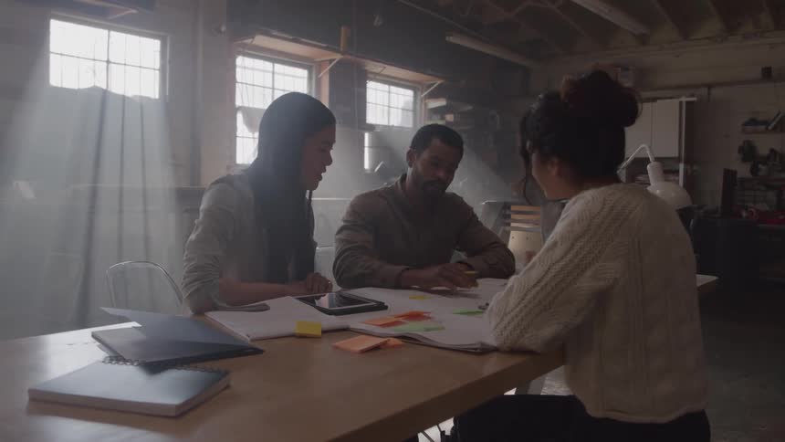 People collaborate at a wooden table with work materials in a sunlit space
