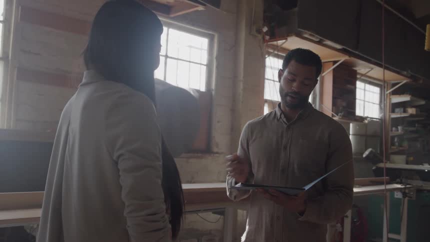 Three people work in a workshop lit by windows with tools and machines in the background