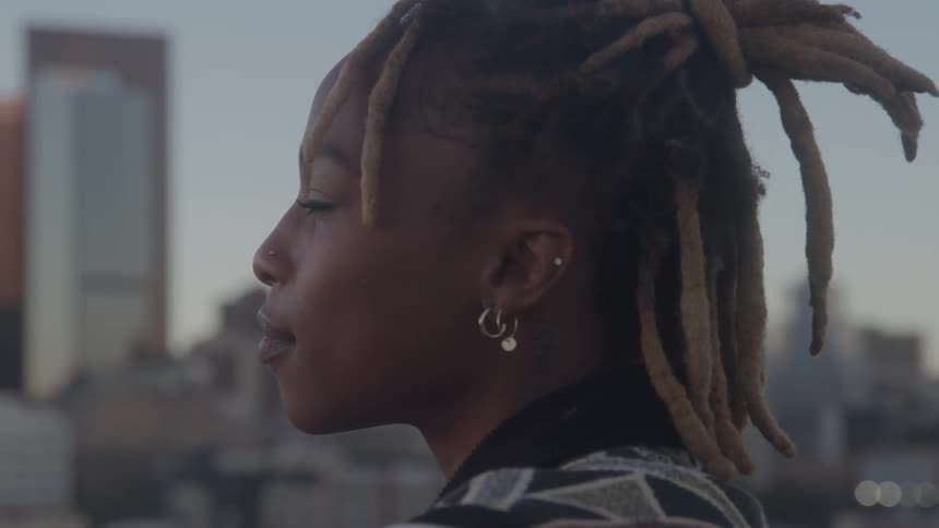 Woman in profile with dreadlocks looks at city in outdoor setting