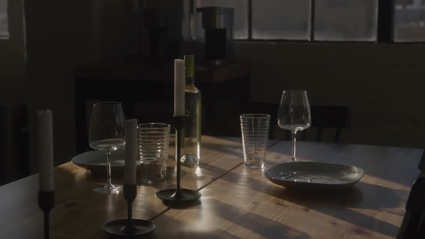 Rustic dining table with wine glasses and candles bathed in soft window light in cozy setting