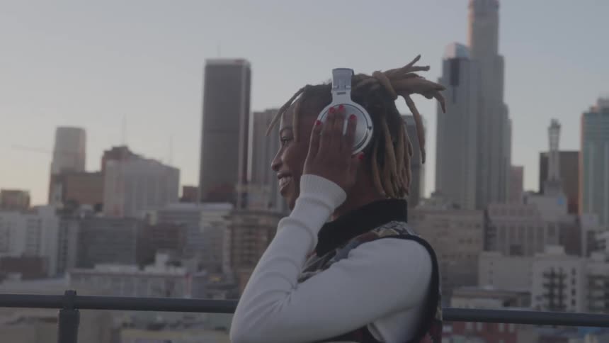 Smiling person with headphones enjoys city view from rooftop at sunset