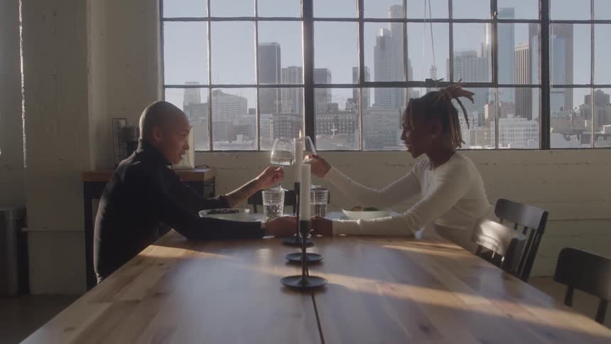 Couple toasts with wine glasses at a set table overlooking the city