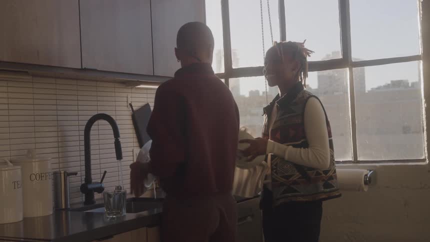 Couple interacts in sunlit kitchen exchanging gestures and words while sharing household tasks in a modern cozy setting