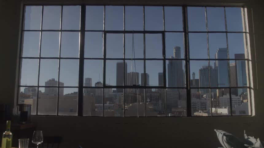 Urban view through industrial window in modern loft with set dining table and soft evening light illuminating the buildings outside