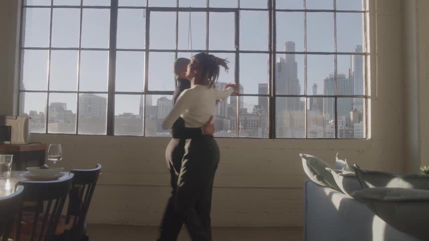 Couple dances together in sunlit room with city view through the windows