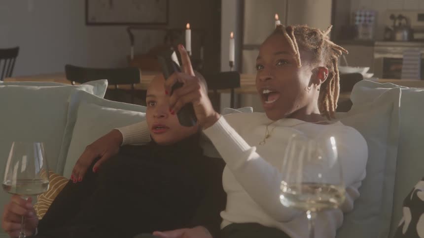 People sitting together on a couch share wine in a candlelit living room