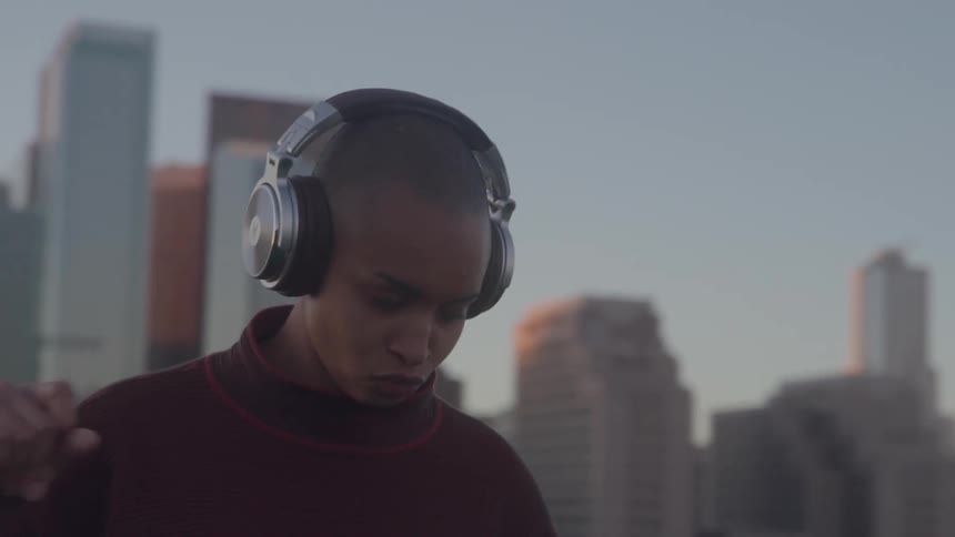 Person listens to music with large headphones while moving in front of tall buildings